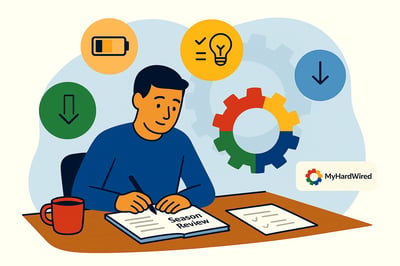 A flat, landscape-style illustration of a person sitting at a wooden desk, writing in a notebook labeled “Season Review.” The person appears calm and reflective. Above and around them float three soft insight icons: a half-full battery representing energy levels, a lightbulb with checkmarks representing wins and lessons, and downward arrows symbolizing drains. Behind the person is a faint MyHardWired gear in red, yellow, blue, and green. A small MyHardWired logo sits in the lower right corner, all set against a soft pastel-blue background.